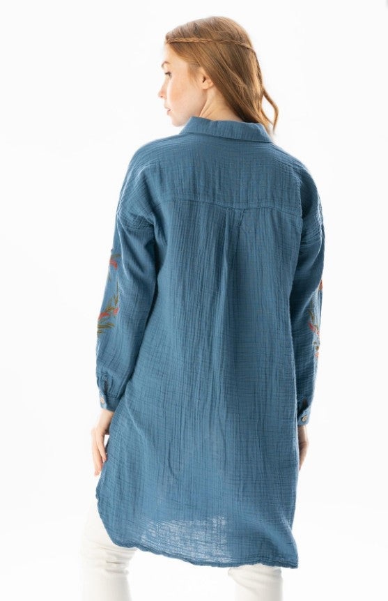 Woman wearing a blue denim shirt with floral embroidery on a white background